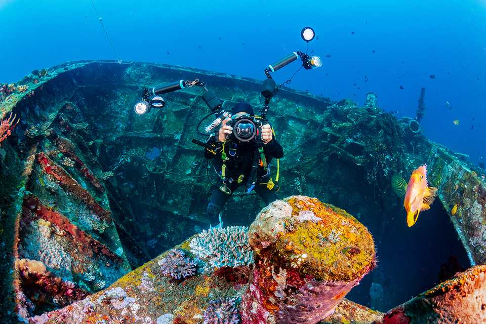 A diver photographs the hull of a sunken ship.