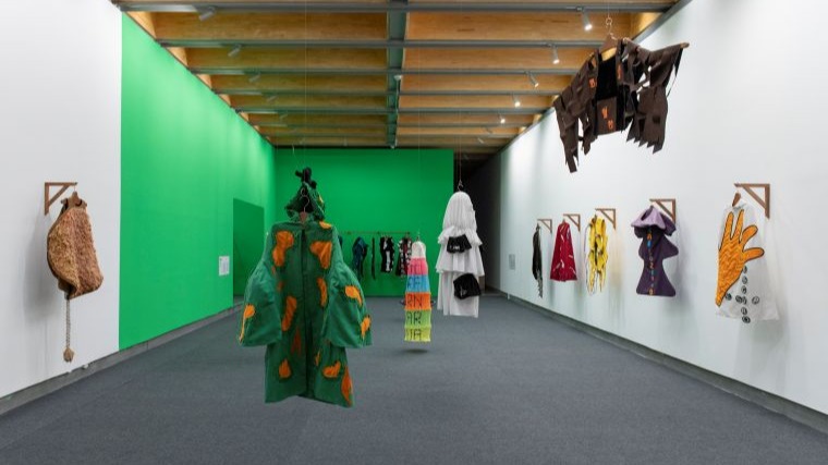 Sala expositiva com diversas capas infantis de tecidos, cores e formatos diferentes.