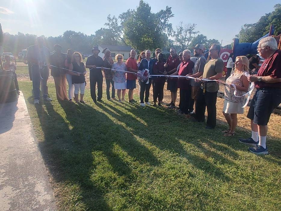 Michigan state Representative Reggie Miller and community members in Romulus holding a string of ribbon in front a playground. Michigan state Representative Reggie Miller and community members in Romulus holding a string of ribbon in front a playground.