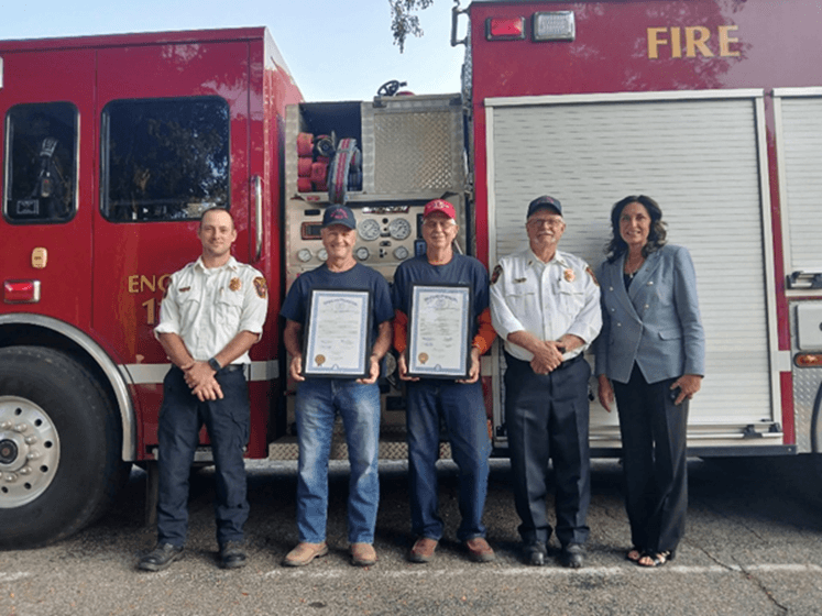Michigan state Representative Angela Witwer and Bellevue Community Fire Department retirees holding tribute certificates in front of a fire truck. Michigan state Representative Angela Witwer and Bellevue Community Fire Department retirees holding tribute certificates in front of a fire truck.