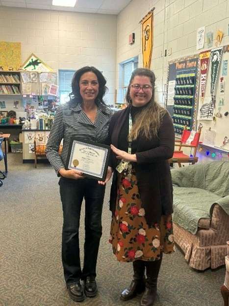 Michigan state Representative Angela Witwer presenting a framed certificate to Maggie Robison in a high school classroom. Michigan state Representative Angela Witwer presenting a framed certificate to Maggie Robison in a high school classroom.