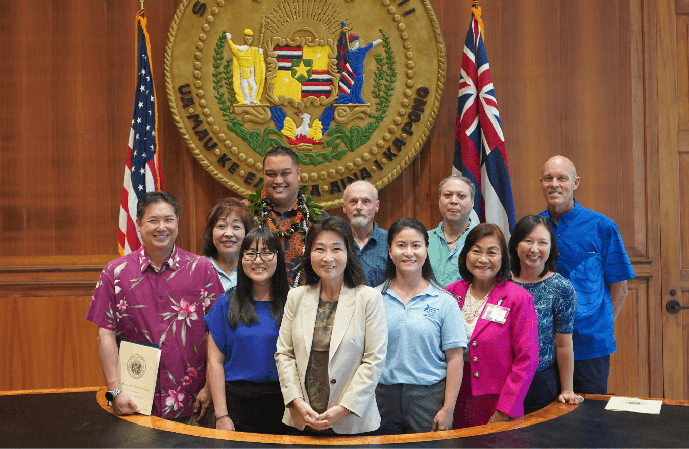 Lt. Gov. Sylvia Luke, legislators, and group smiling for a group picture in front of the Hawaiʻi State Seal. 