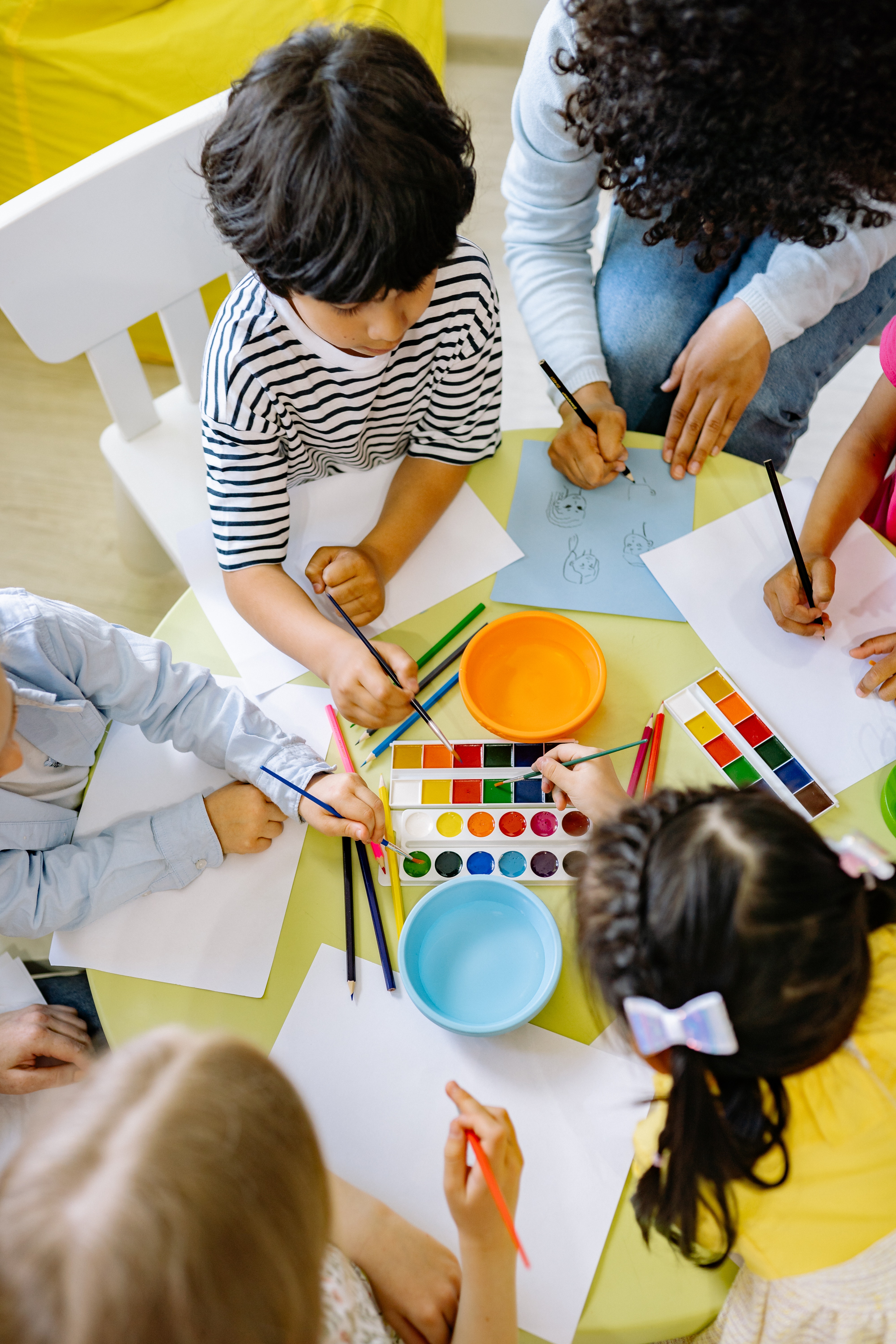 Children sitting at a table while dipping paint brushes in paint. 