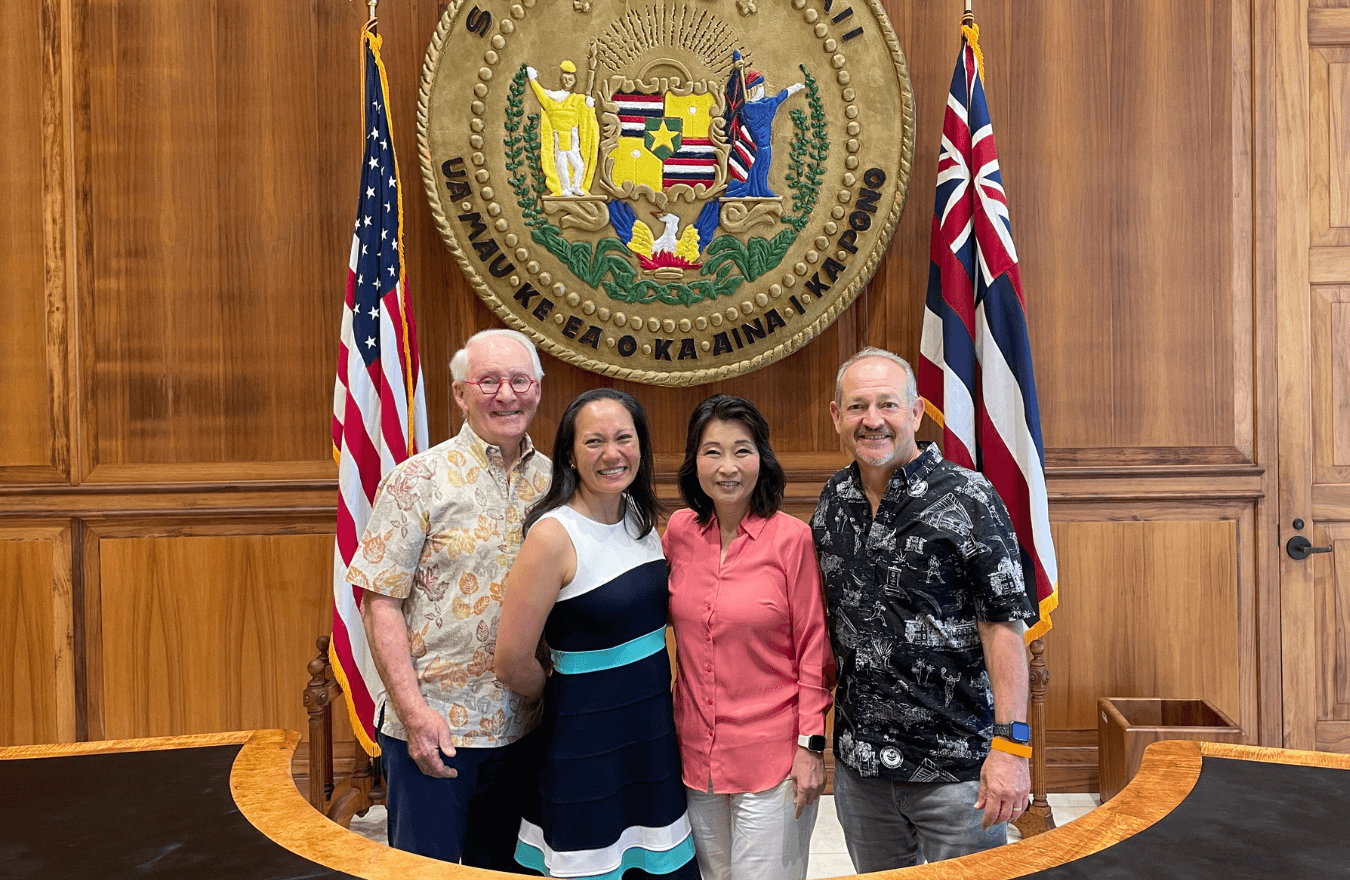 Lt. Gov. Sylvia Luke and group smiling for a group picture in front of the Hawaiʻi State Seal. 