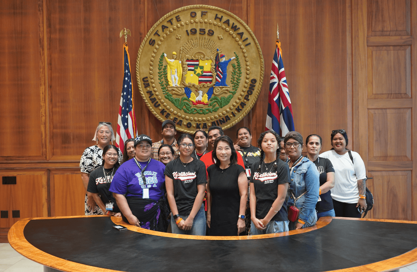 Lt. Gov. Sylvia Luke, a legislator, and group smiling for a group picture in front of the Hawaiʻi State Seal. 
