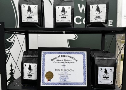 A photo of a shelf of bagged coffee and a framed certificate from the Michigan House of Representatives dedicated to Wild Wolf Coffee. A photo of a shelf of bagged coffee and a framed certificate from the Michigan House of Representatives dedicated to Wild Wolf Coffee.