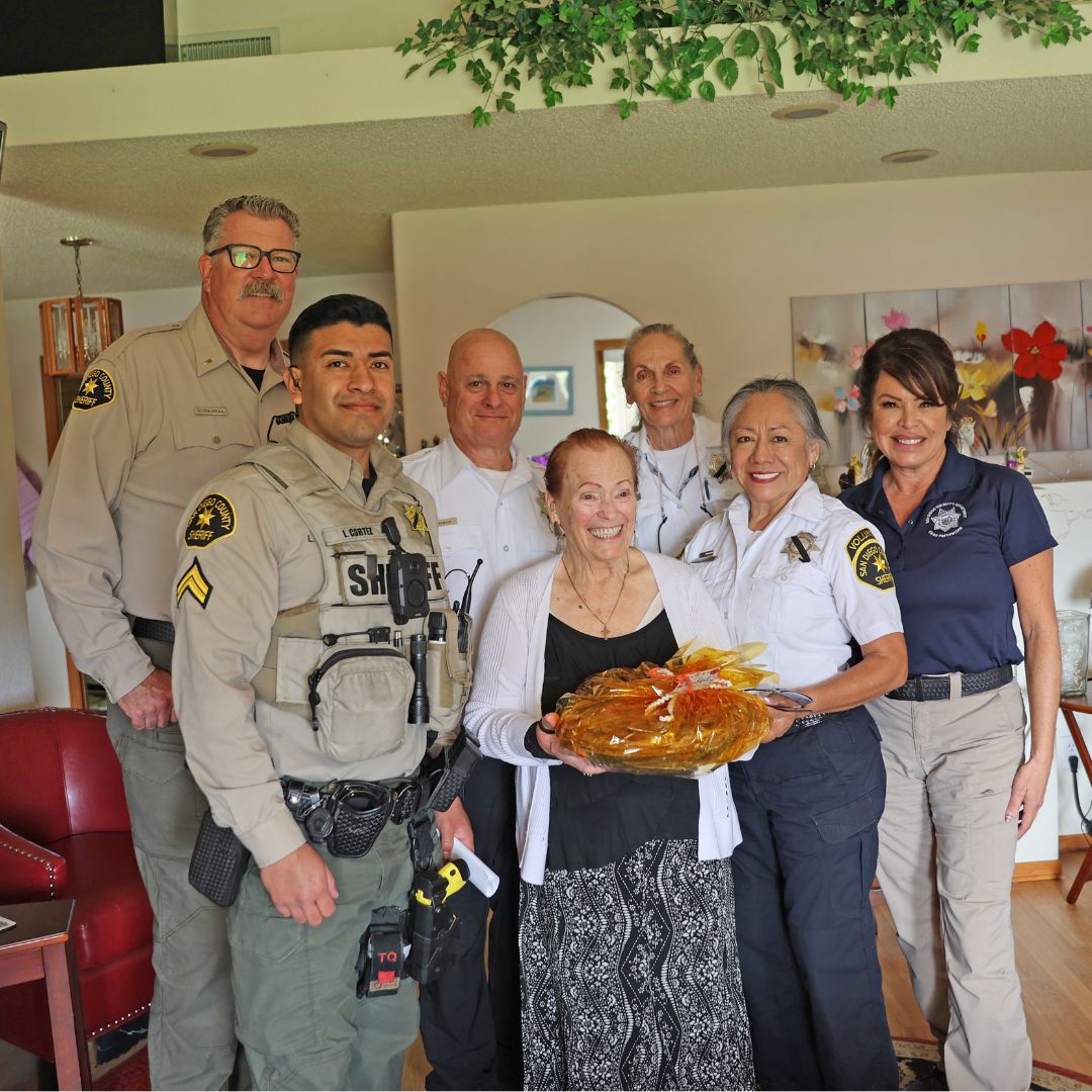 Yana program photo with two deputies and Sheriff Senior Patrol with a crime prevention specialist inside someone's home with an elderly women holding a pie.