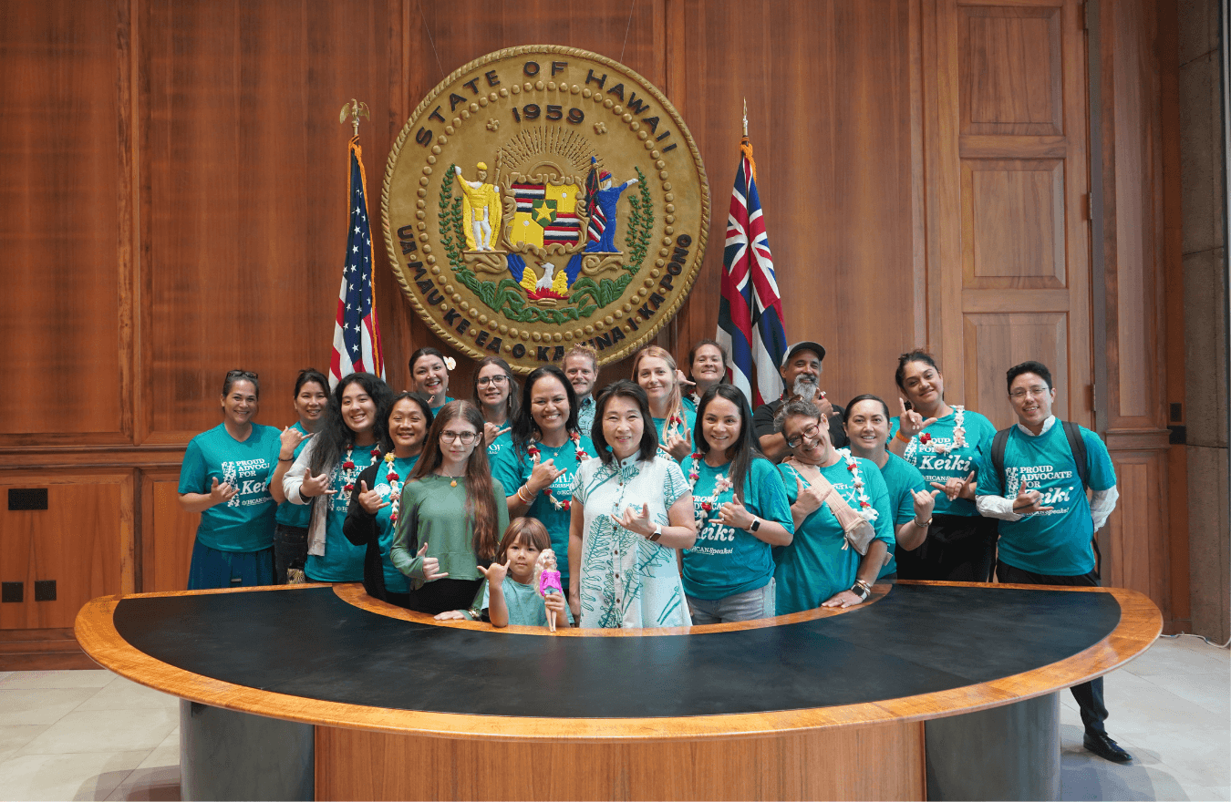 Lt. Gov. Sylvia Luke group smiling for a group photo in front of the Hawaiʻi State Seal. 