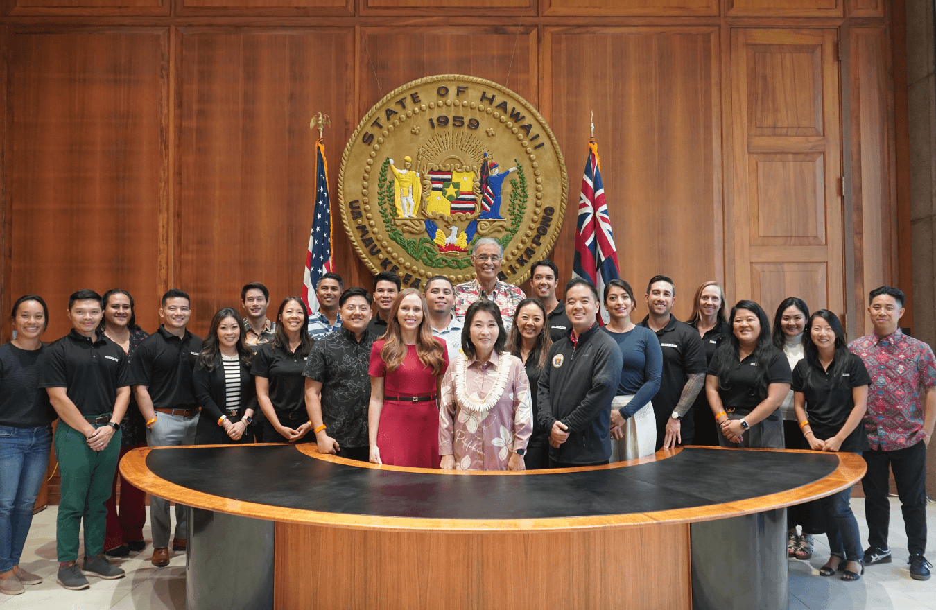 Lt. Gov. Sylvia Luke, legislators, and group smiling for a group photo in front of the Hawaiʻi State Seal. 