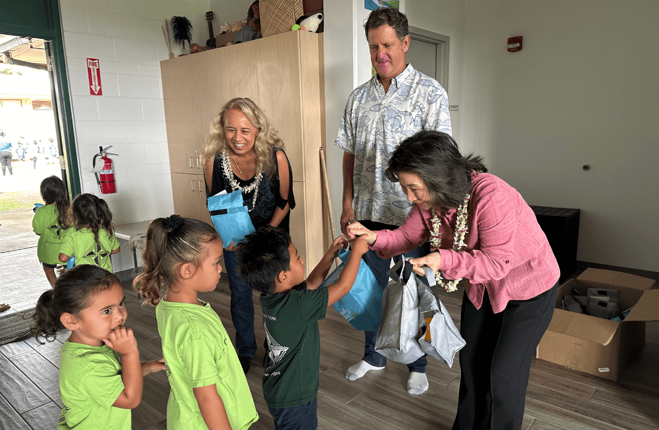 Lt. Gov. Sylvia Luke and legislator smiling while handing out blue and grey lunchboxes to pre-k students in a Ready Keiki classroom. 