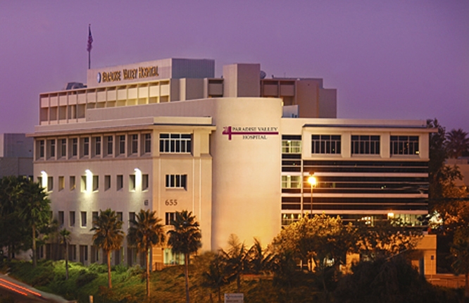 A person taking a breathalizer test to see alcohal level. shows a car in the back with a machine being held with blue sticker with yellow xl type.