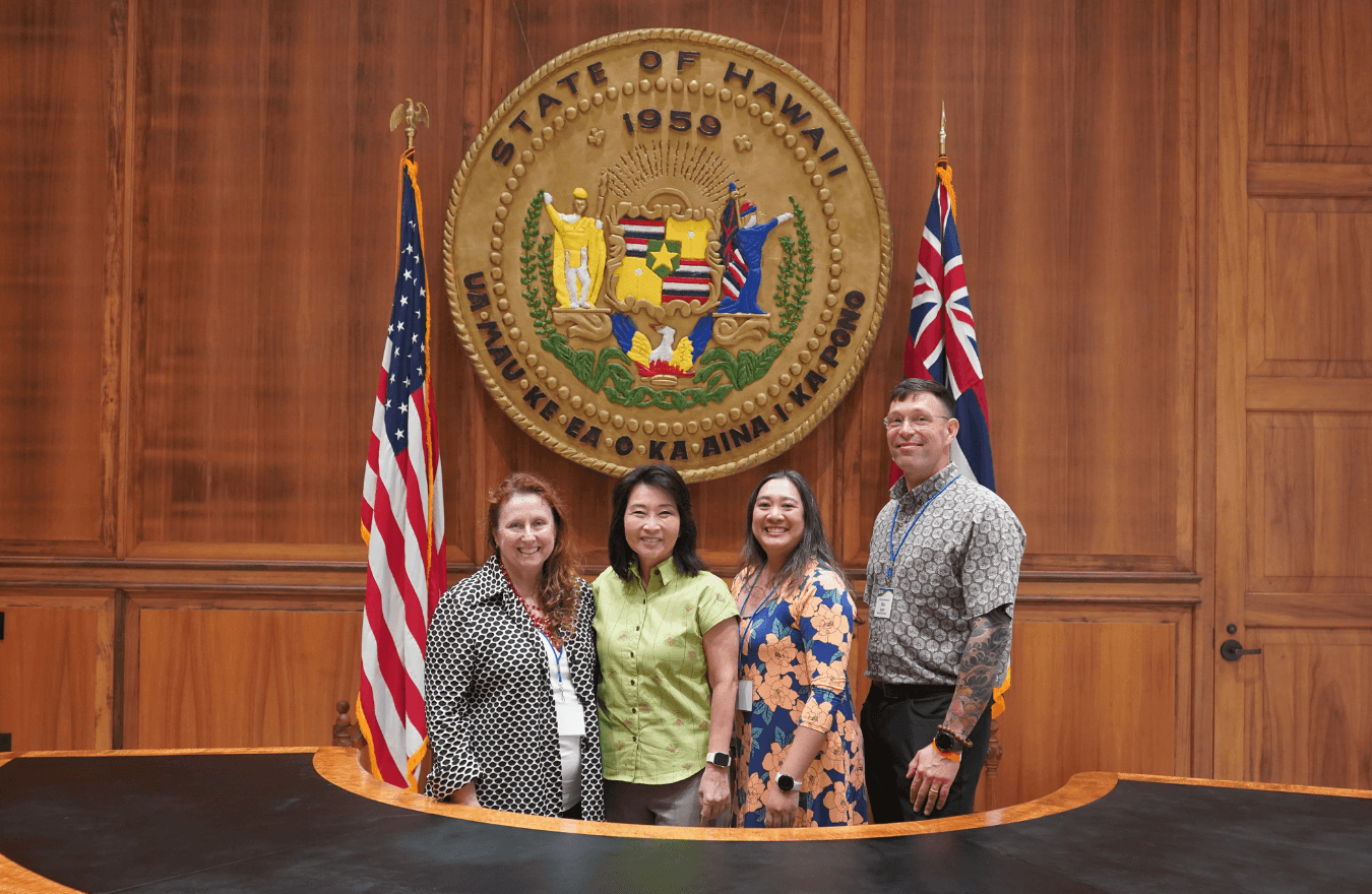 Lt. Gov. Sylvia Luke and group smiling for a group photo in front of the Hawaiʻi State Seal.