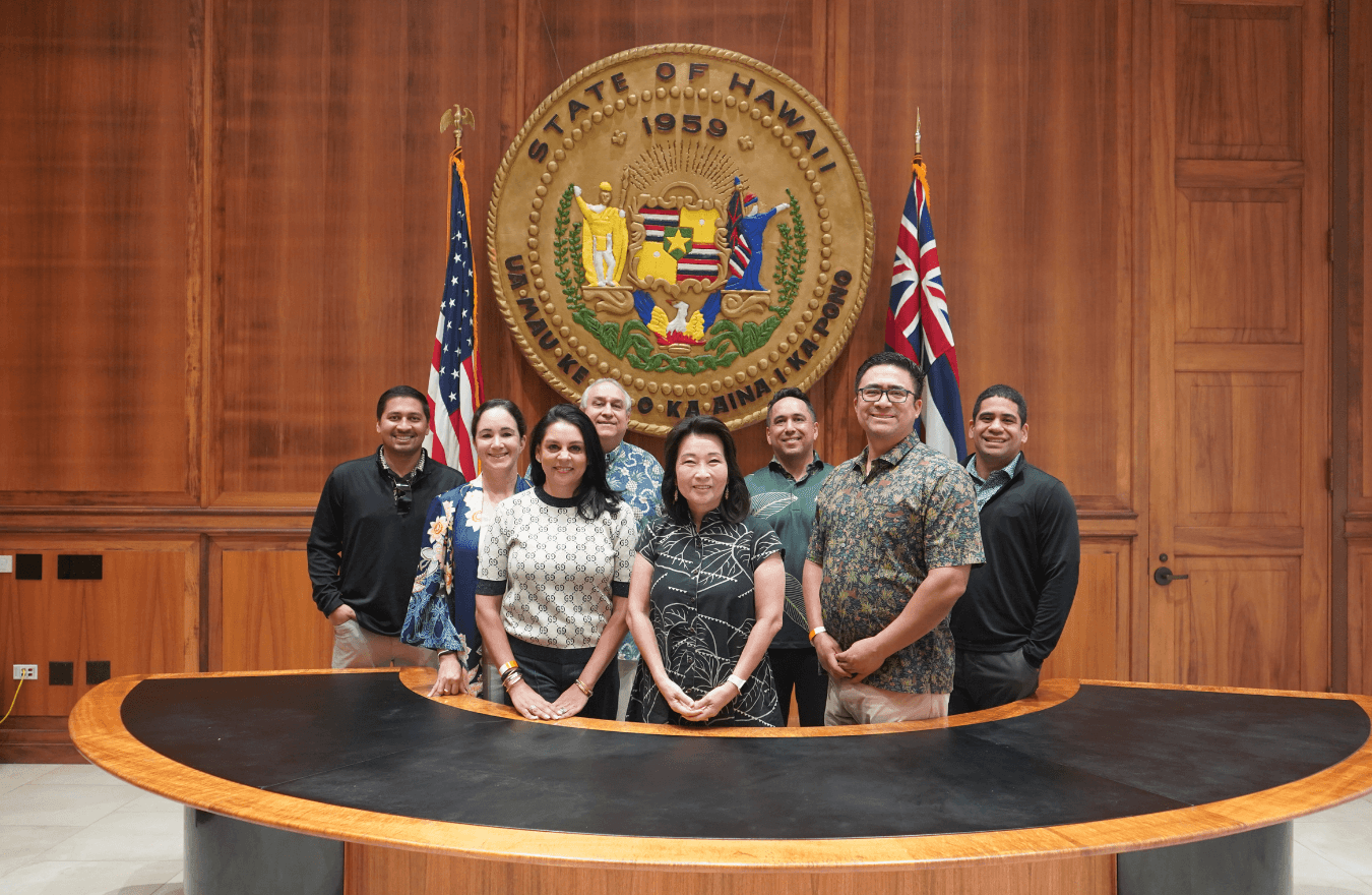 Lt. Gov. Sylvia Luke and group smiling for a group photo in front of the Hawaiʻi State Seal. 