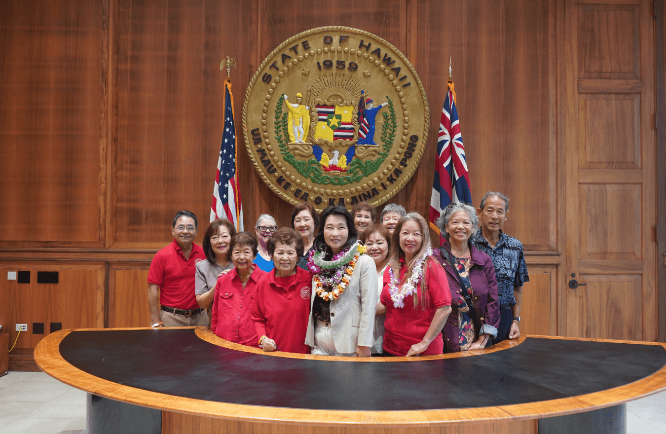 Lt. Gov. Sylvia Luke and group smiling for a group photo in front of the Hawaiʻi State Seal. 