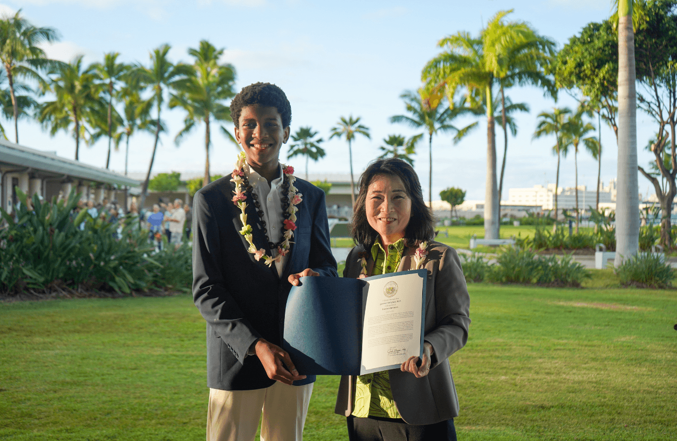 Lt. Gov. Sylvia Luke and a boy smiling for a photo while holding open a certificate folder. 