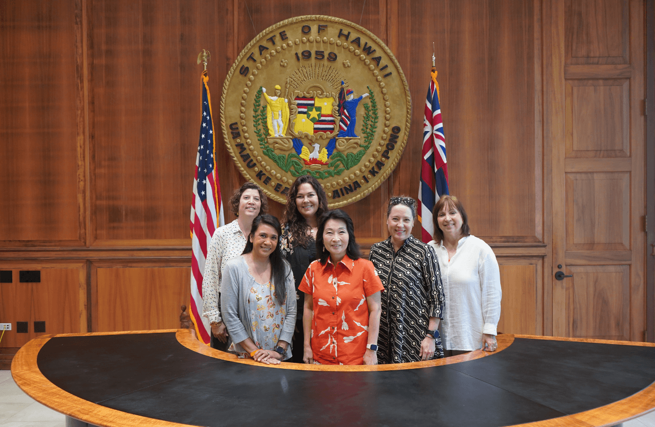 Lt. Gov. Sylvia Luke and group smiling for a group photo in front of the Hawaiʻi State Seal. 