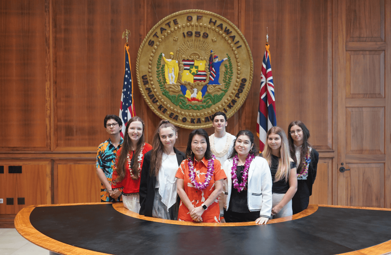 Lt. Gov. Sylvia Luke and a group of students smiling for a group photo in front of the Hawaiʻi State Seal. 