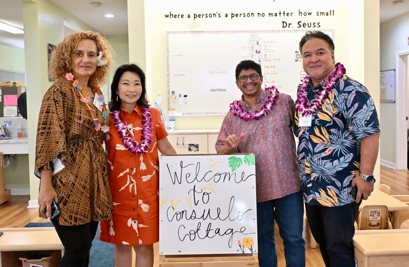 Lt. Gov. Sylvia Luke and group smiling for a group photo with a sign saying, “Welcome to Consuelo Cottage.” 