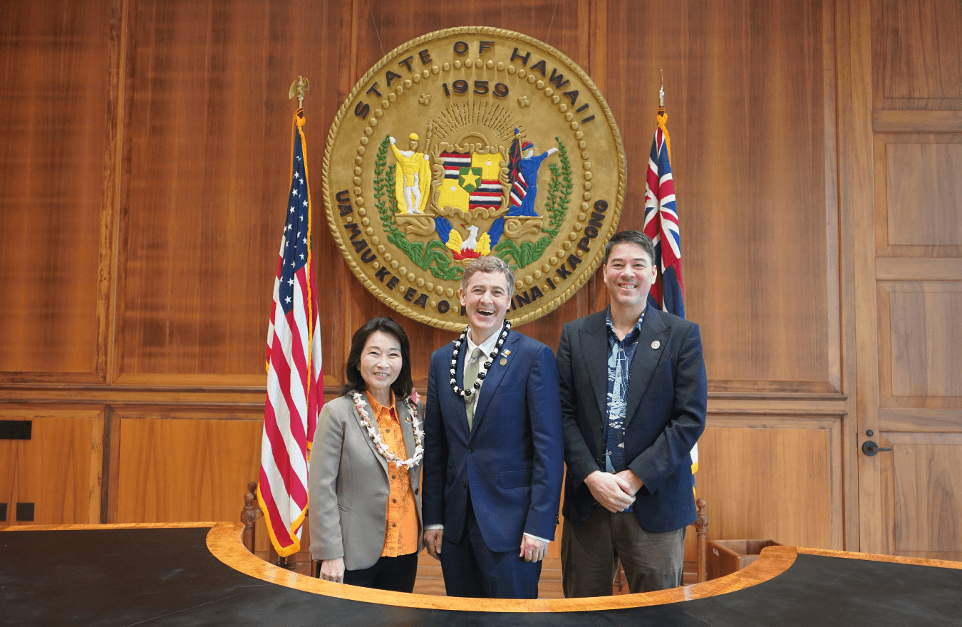 Lt. Gov. Sylvia Luke and group smiling for a group photo in front of the Hawaiʻi State Seal. 