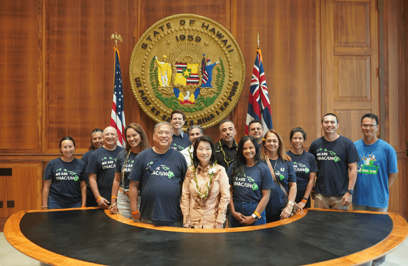 Lt. Gov. Sylvia Luke and group smiling for a group photo in front of the Hawaiʻi State Seal. 
