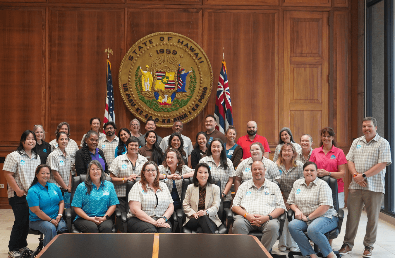 Lt. Gov. Sylvia Luke and group smiling for a group photo in front of the Hawaiʻi State Seal. 