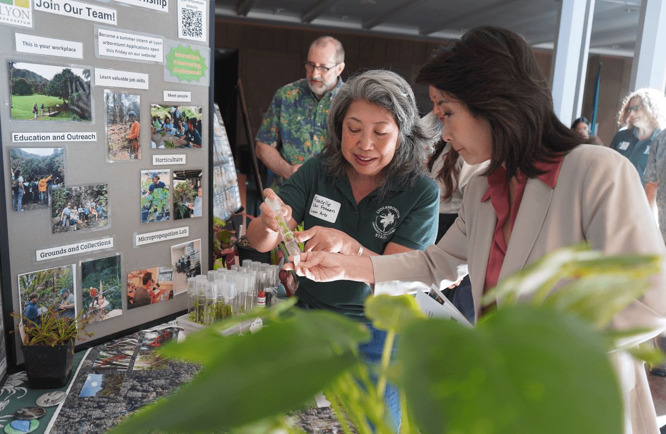Lt. Gov. Sylvia Luke and a lady looking at a test tube while pointing to a plant inside of it. 