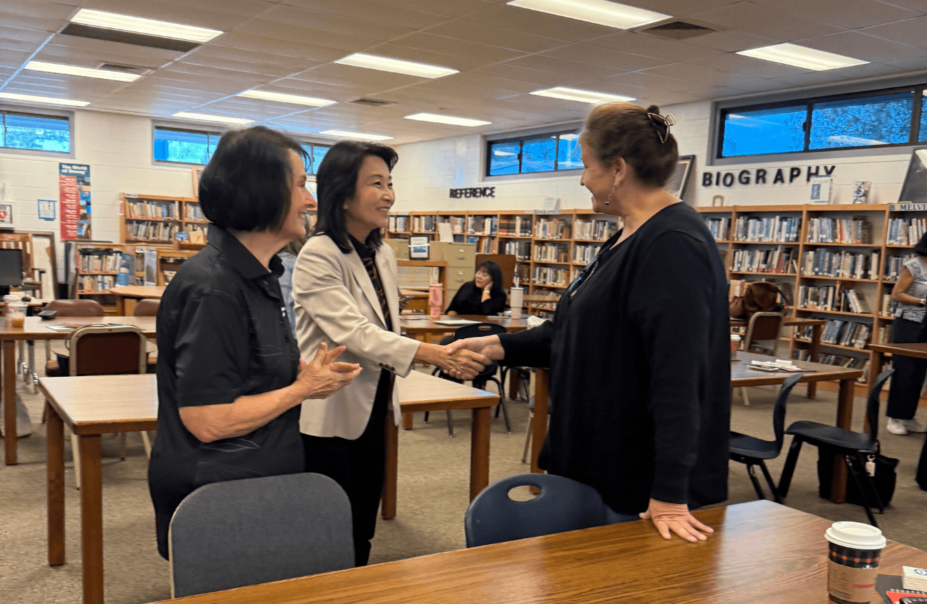 Lt. Gov. Sylvia Luke smiling while shaking a lady’s hand and standing next to another smiling lady in a library. 