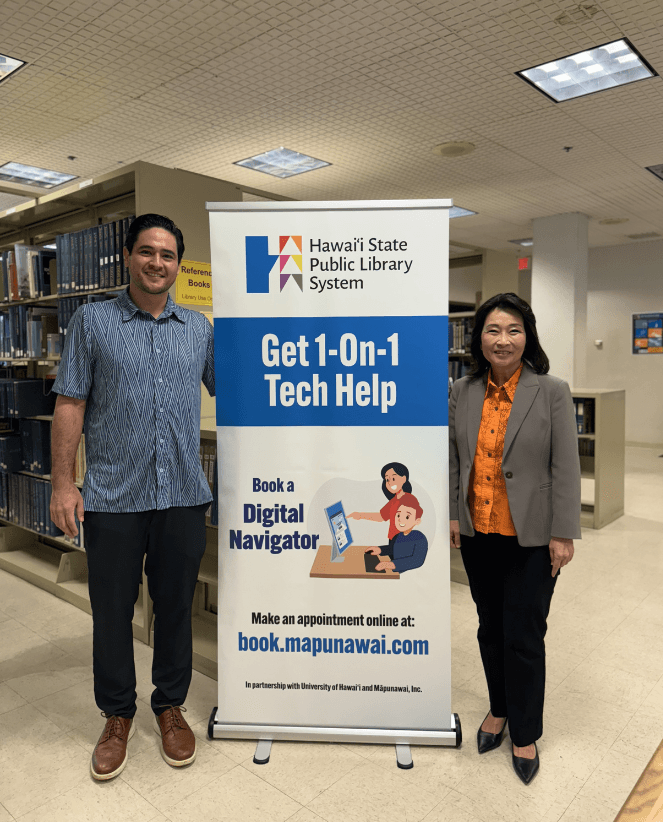 Lt. Gov. Sylvia Luke and a man standing with a banner in between them in a library. 