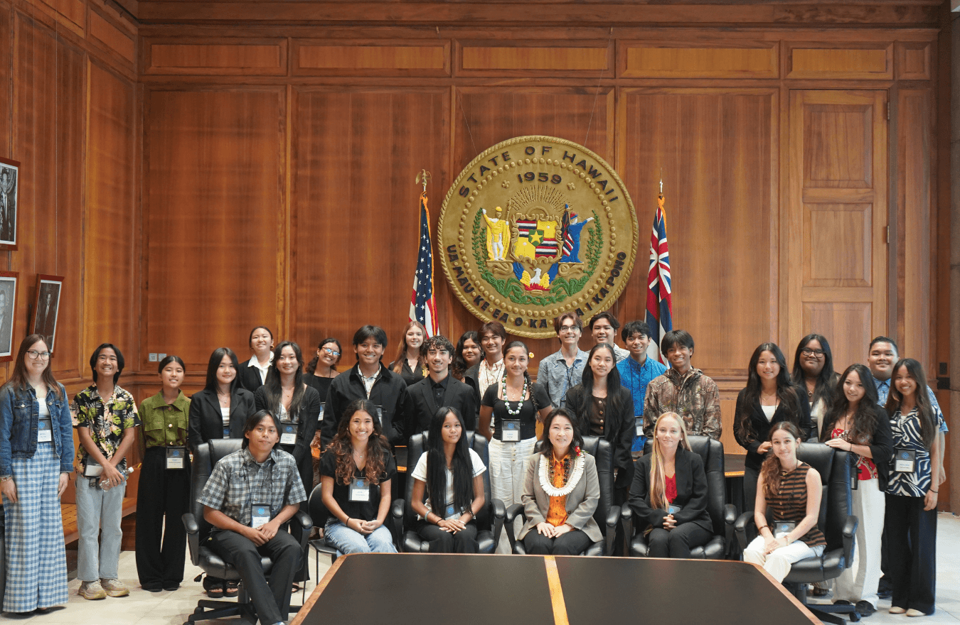 Lt. Gov. Sylvia Luke and a large group smiling for a group photo in front of the Hawaiʻi State Seal. 
