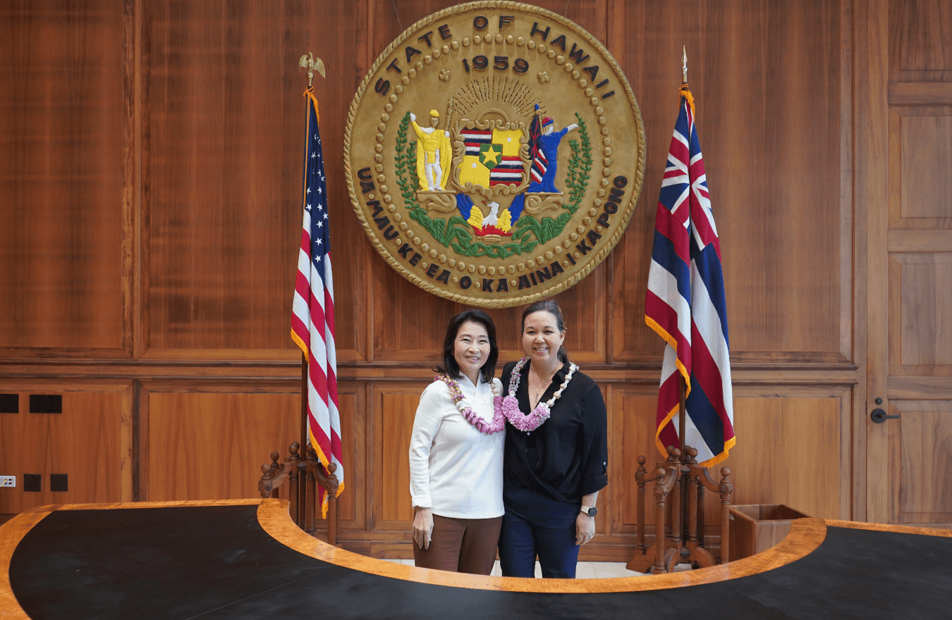 Lt. Gov. Sylvia Luke and a woman smiling for a photo in front of the Hawaiʻi State Seal. 