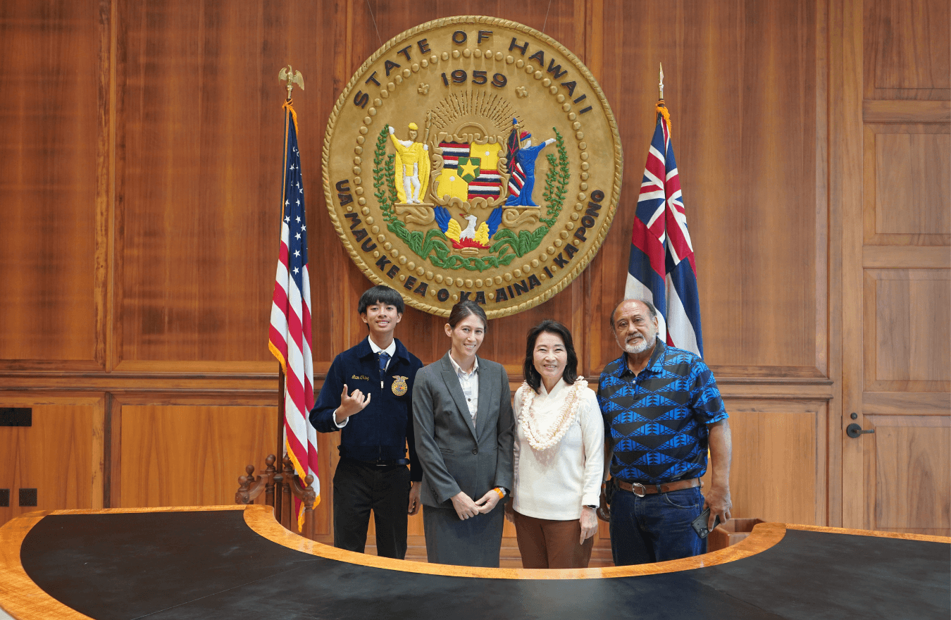 Lt. Gov. Sylvia Luke and group smiling for a group photo in front of the Hawaiʻi State Seal. 