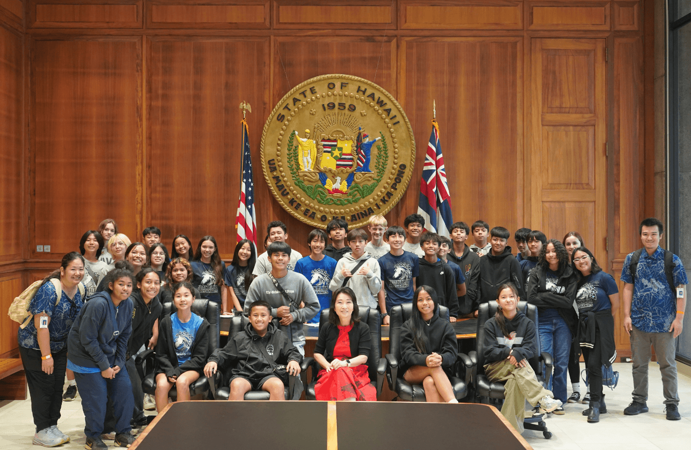 Lt. Gov. Sylvia Luke and a large group smiling for a group photo in front of the Hawaiʻi State Seal. 