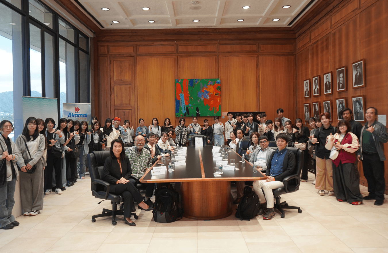 Lt. Gov. Sylvia Luke smiling while sitting at a large table with a group with more people stand around them, also smiling for a group photo. 