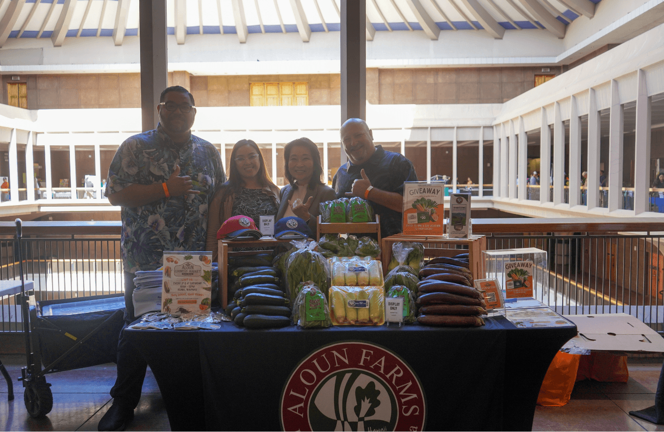 Lt. Gov. Sylvia Luke and group smiling while holding up shakas for a group photo with produce on a table in front of them. 