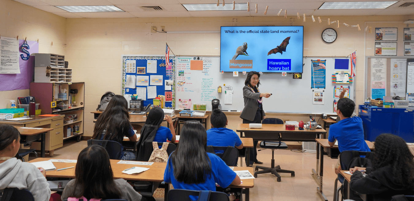 Lt. Gov. Sylvia Luke in a classroom smiling and pointing to a student with their hand raised. 