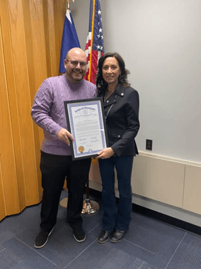Michigan state Representative Angela Witwer presenting a framed tribute certificate to Michael Armitage. Michigan state Representative Angela Witwer presenting a framed tribute certificate to Michael Armitage.