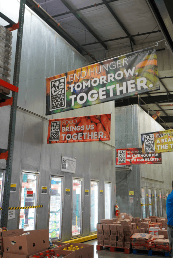 Signs in a warehouse with industrial refrigerators that says, “End hunger tomorrow. Together” and “Food brings us together.” 