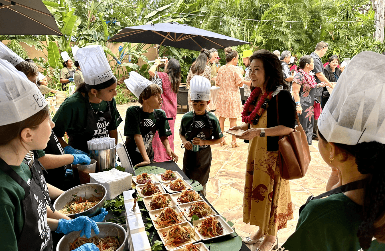 Lt. Gov. Sylvia Luke smiling while talking to kids wearing chef hats in front of a table with food. 