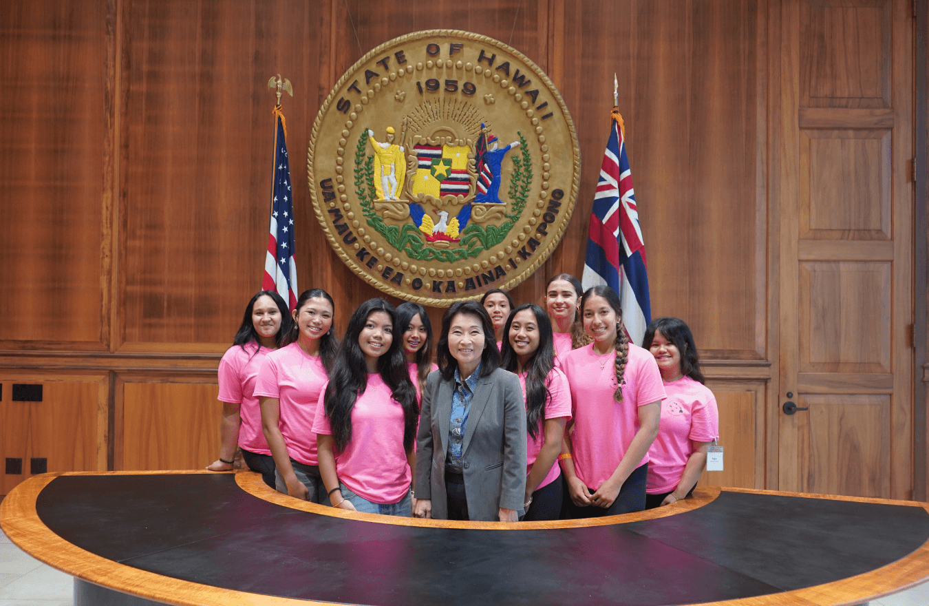 Lt. Gov. Sylvia Luke and group smiling for a group photo in front of the Hawaiʻi State Seal. 
