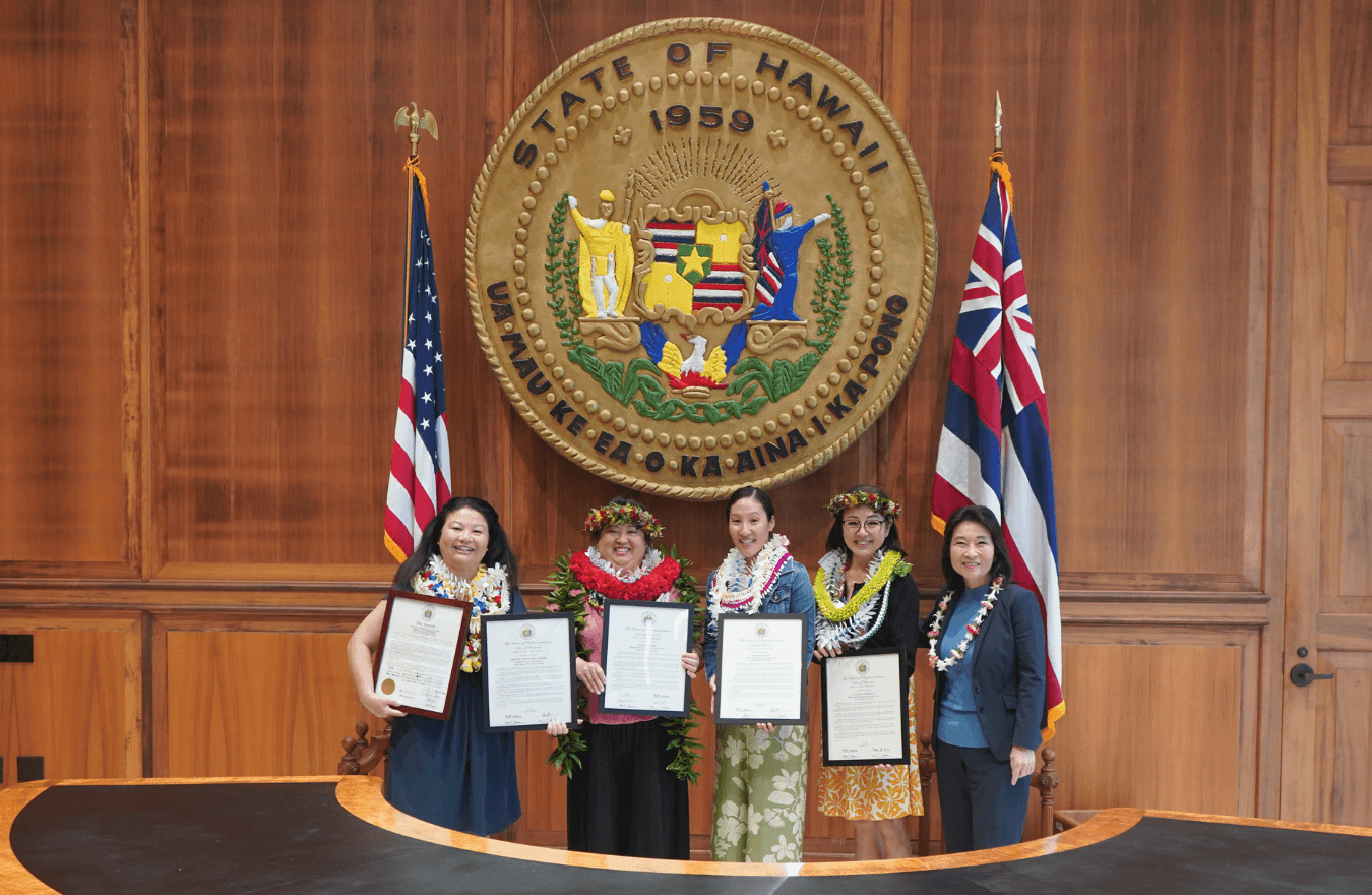 Lt. Gov. Sylvia Luke and group smiling for a group photo in front of the Hawaiʻi State Seal. 