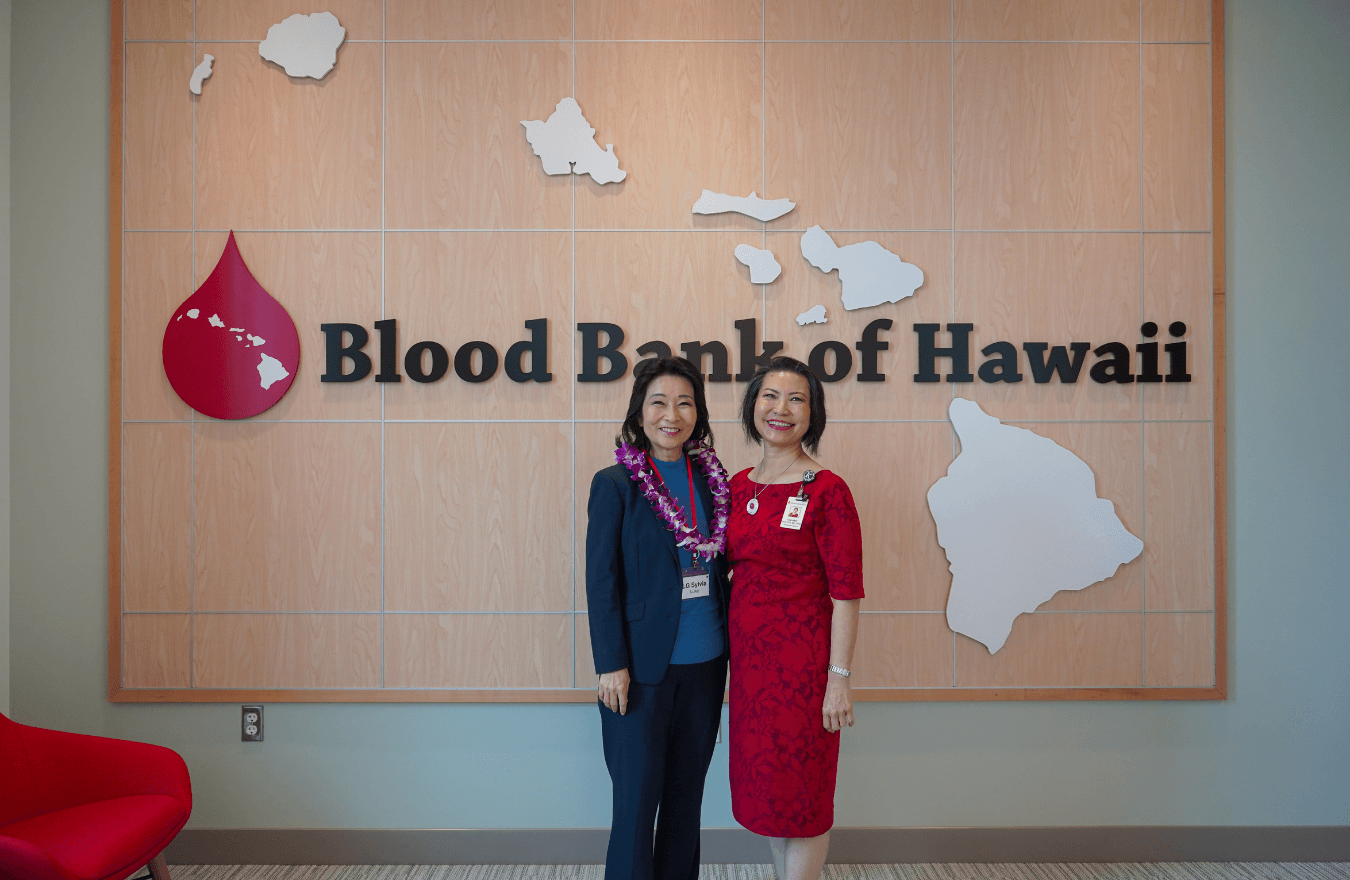 Lt. Gov. Sylvia Luke and lady smiling for a photo in front of a sign that says, “Blood Bank of Hawaii.” 