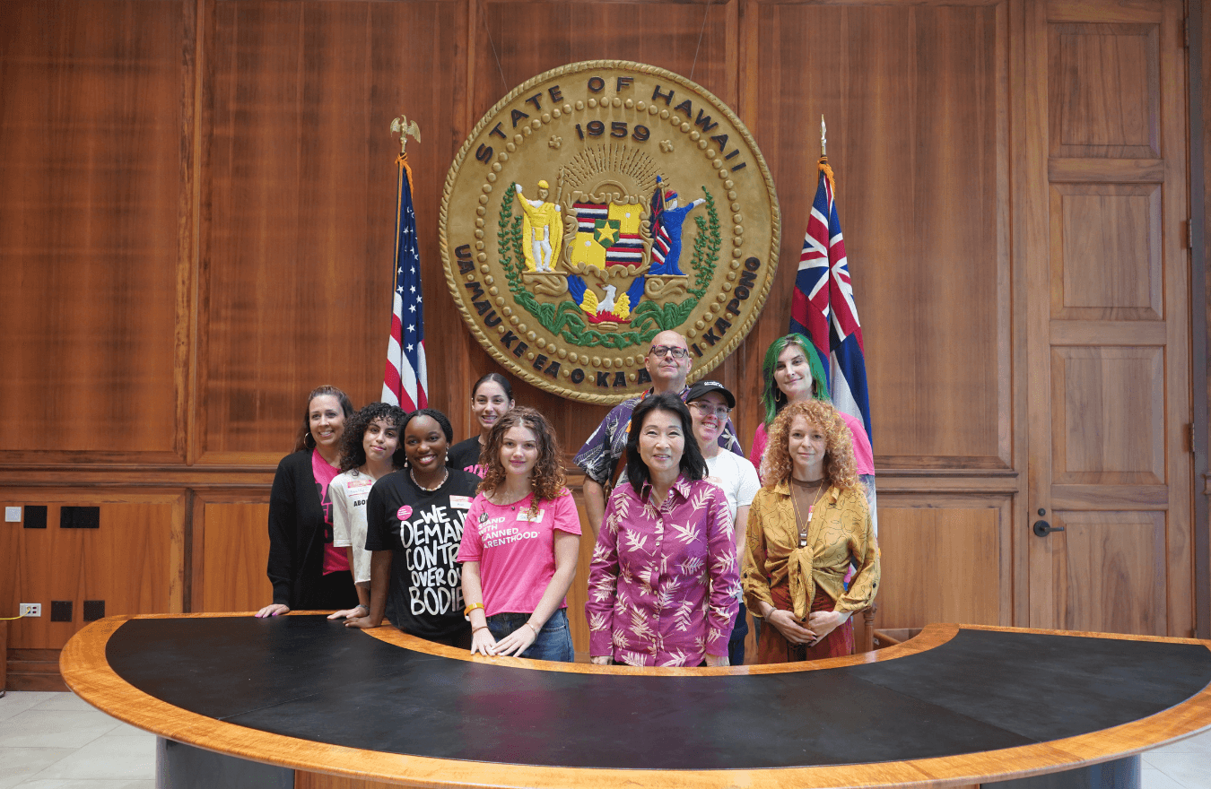 Lt. Gov. Sylvia Luke and group smiling for a group photo in front of the Hawaiʻi State Seal. 