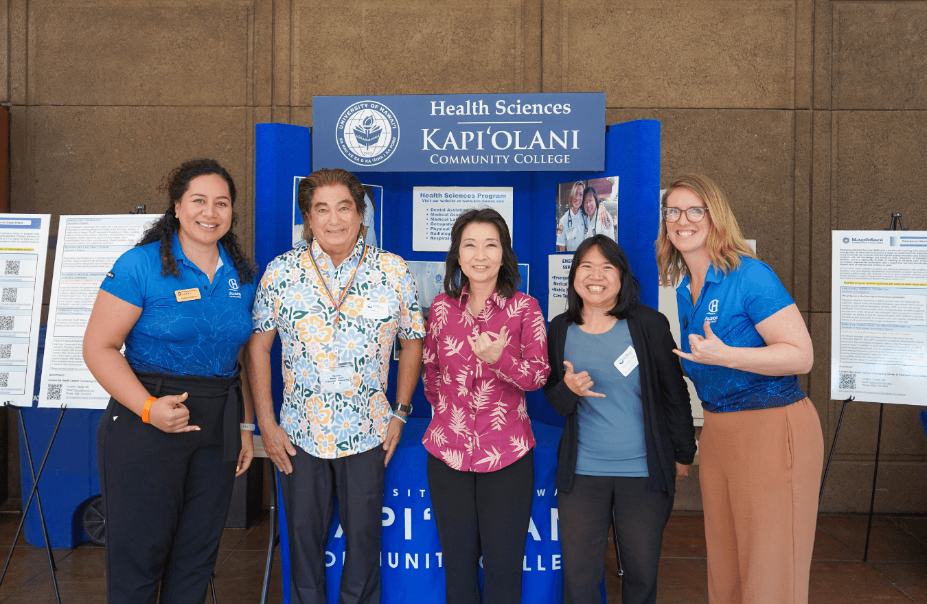 Lt. Gov. Sylvia Luke and group smiling while holding up shakas for a group photo in front of a presentation board that says, “Health Sciences Kapiʻolani Community College.” 