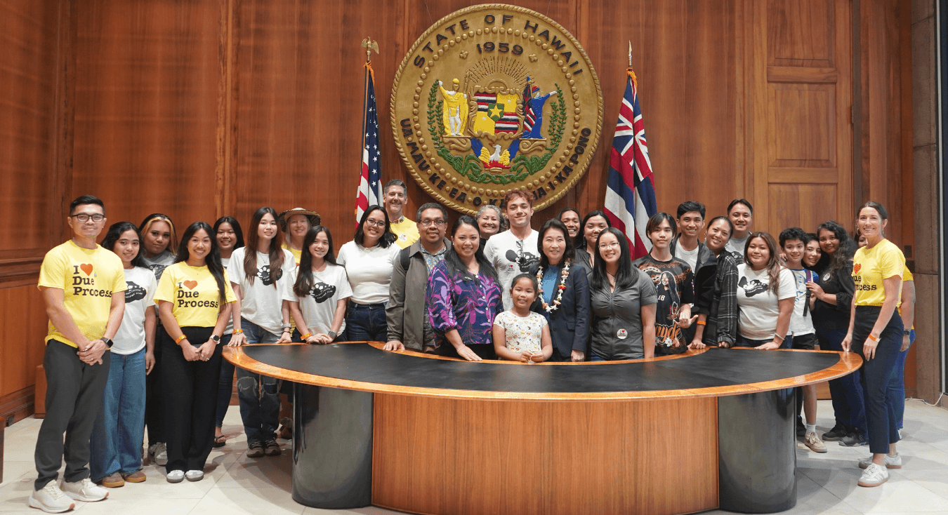 Lt. Gov. Sylvia Luke and group smiling for a group photo in front of the Hawaiʻi State Seal. 