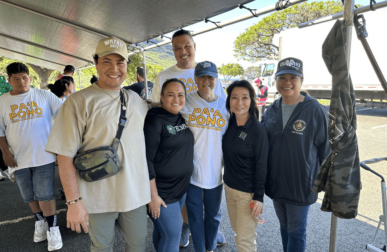 Lt. Gov. Sylvia Luke, a legislator, and group smiling for a group photo in a parking lot under a large tent. 