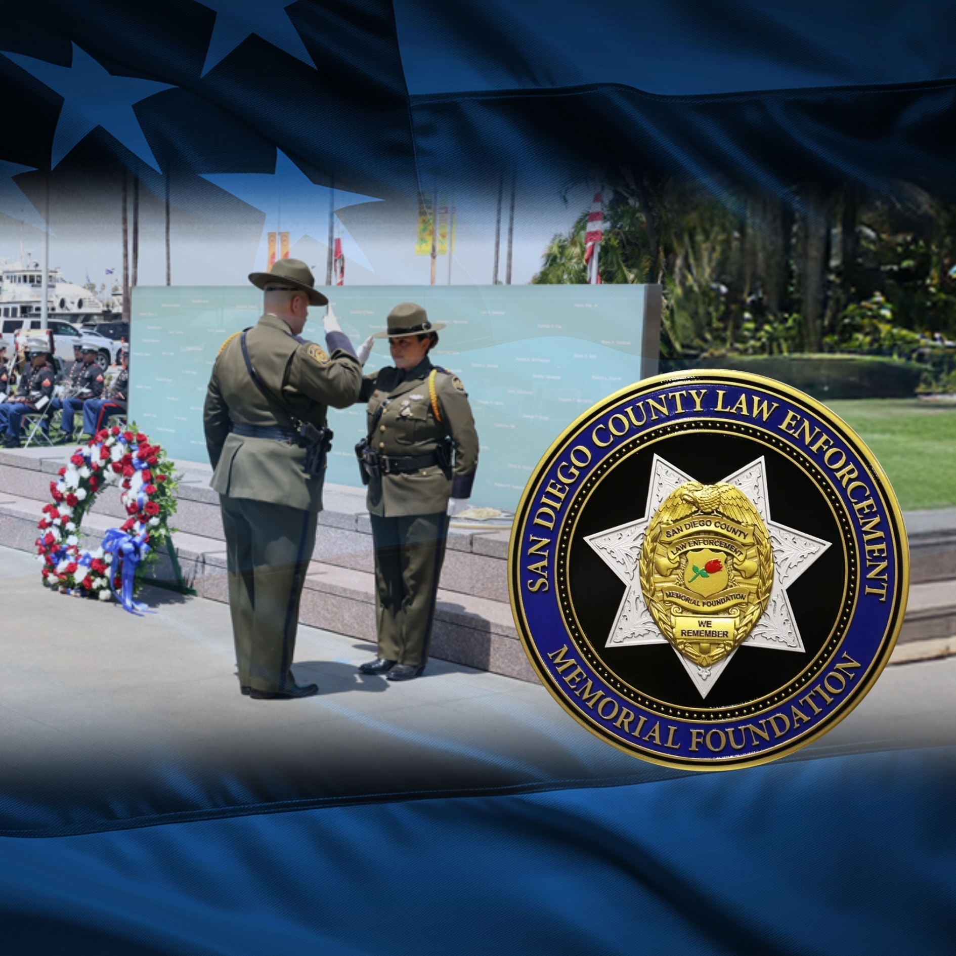 A ceremonial scene at an outdoor law enforcement memorial, where two uniformed honor guard members stand before a large engraved memorial wall. One individual raises a hand in a formal salute. A wreath decorated with red, white, and blue flowers is positioned beside the wall. In the foreground, a badge‑shaped emblem displays the text “San Diego County Law Enforcement Memorial Foundation.” An overlay of a dark blue American flag with stars frames the composition.