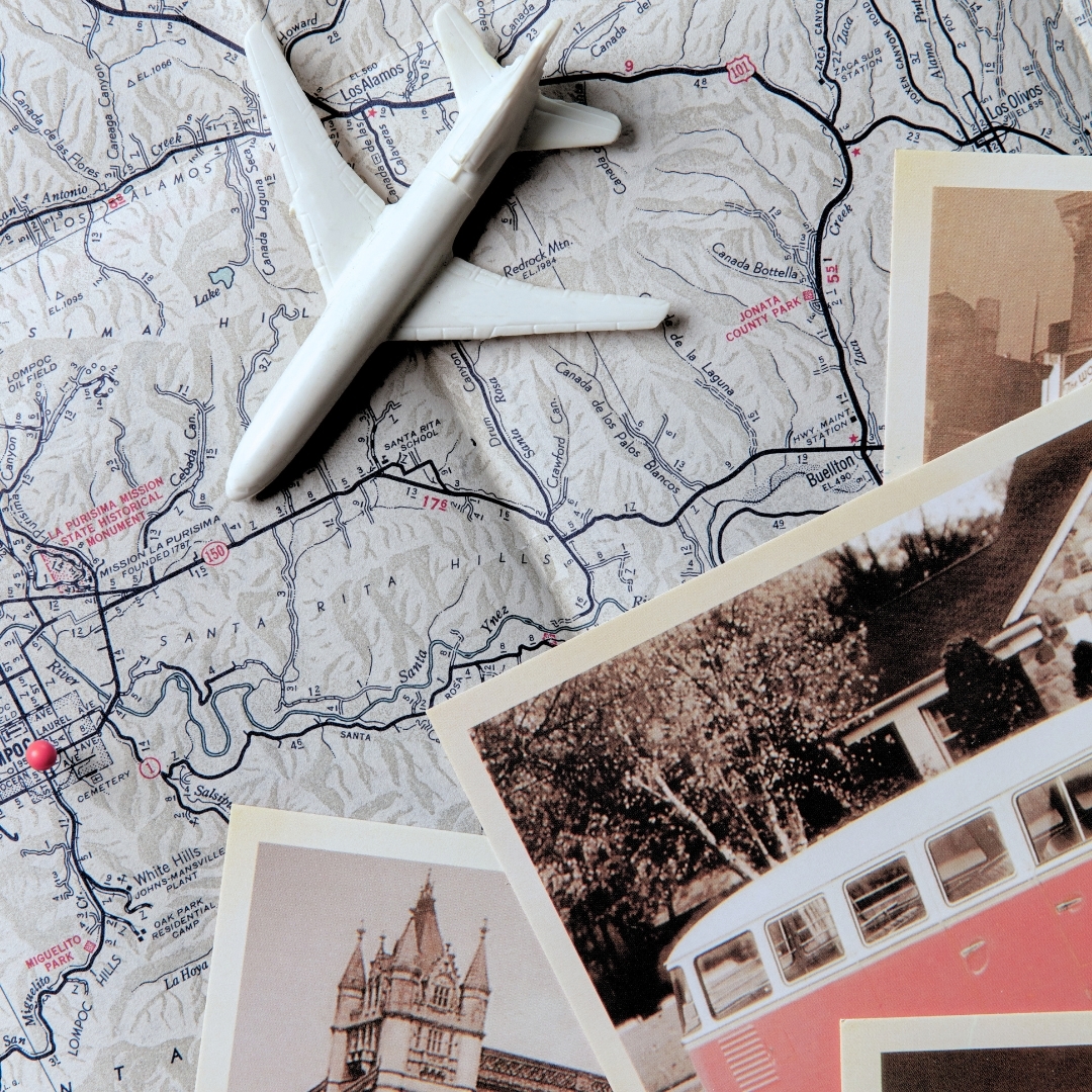 A white toy airplane sits on top of a detailed road map marked with highways and terrain lines. Several vintage-style travel photos, including an image of a building and a red bus, are scattered around the map.