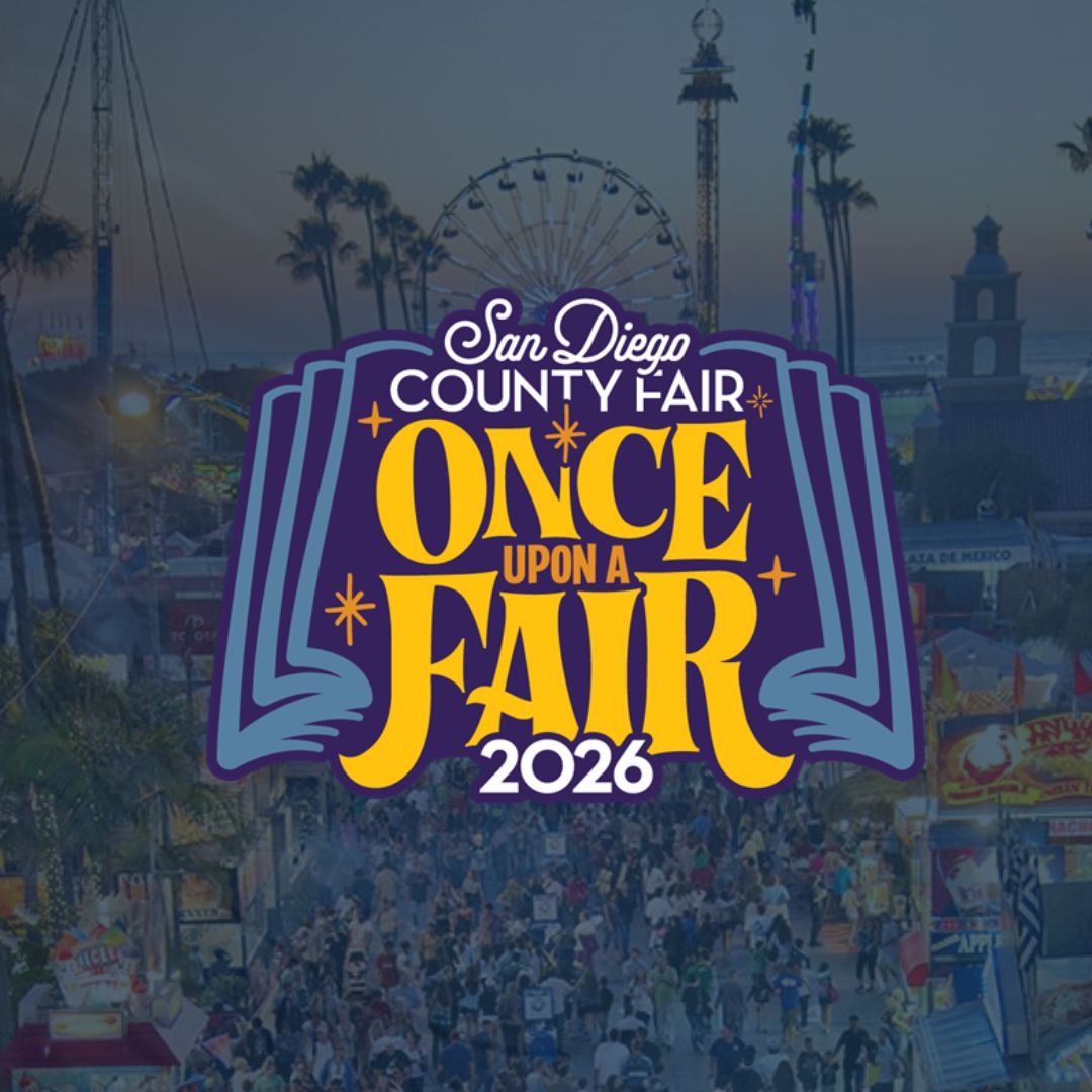 A graphic featuring the text “San Diego County Fair – Once Upon a Fair 2026” displayed in bold, colorful lettering. The background shows a blurred fairground scene with rides, lights, and crowds.