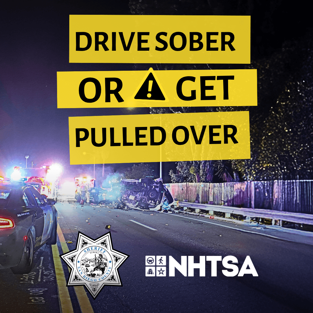  A roadway scene at night with emergency vehicle lights illuminating the area. Bold yellow text in the center reads “Drive Sober or Get Pulled Over.” Logos for a law enforcement agency and NHTSA appear at the bottom of the image.