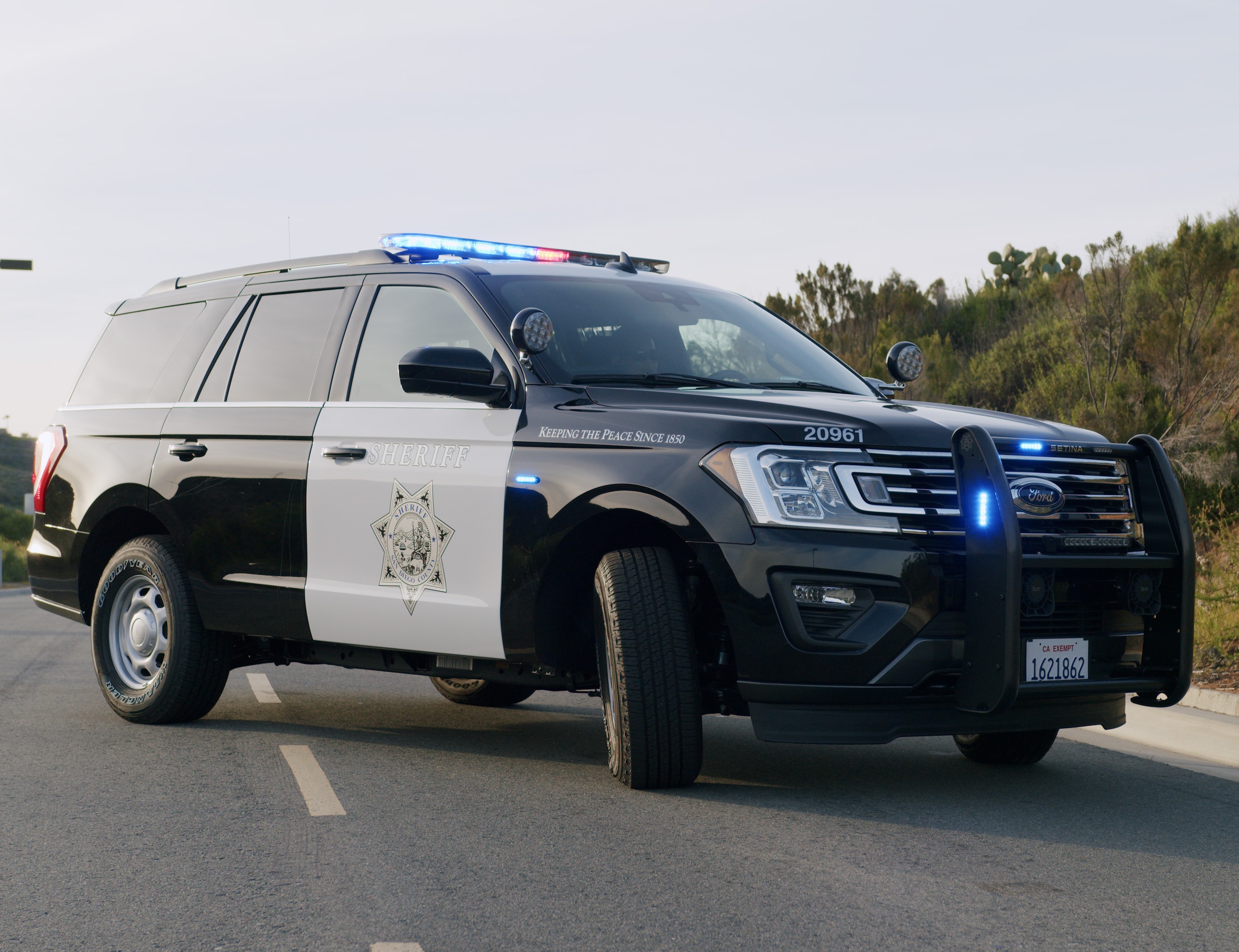 Two san diego county sheriff's office vehicles outside driving in a neighborhood with the patrol lights on.